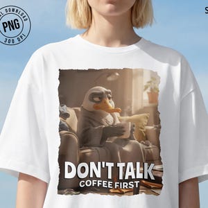 May include: White t-shirt featuring a cartoon duck character holding a coffee cup, with the text "DON'T TALK COFFEE FIRST". The duck is sitting on a couch, wrapped in a blanket. The image has a digital download PNG logo.