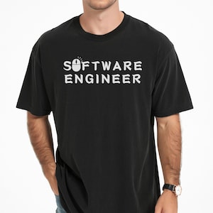 May include: A black short-sleeved t-shirt featuring the white text "SOFTWARE ENGINEER" printed on the chest. The letter "O" in the word "SOFTWARE" is replaced by a white computer mouse icon with a small radiating light graphic above it.