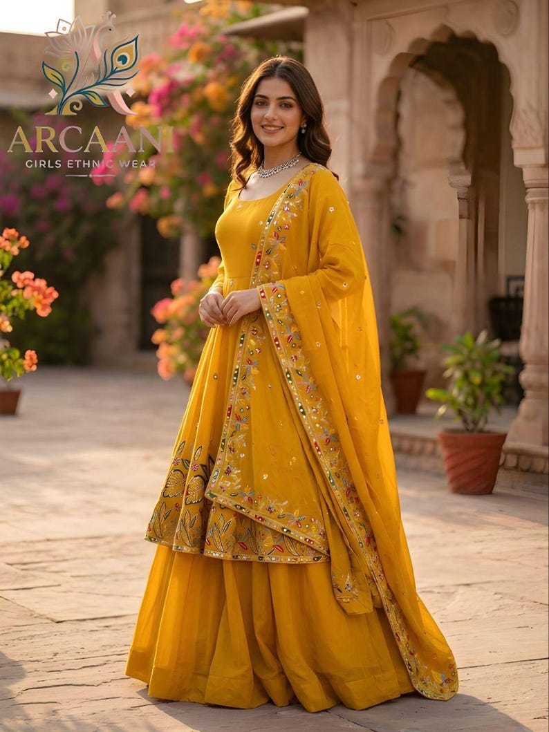 Puede incluir: Una mujer con un atuendo &eacute;tnico amarillo brillante. El conjunto incluye una falda larga y fluida, una blusa con bordados intrincados y una bufanda a juego. El atuendo est&aacute; adornado con bordados y adornos coloridos. El texto "ARCAANI GIRLS ETHNIC WEAR" es visible.