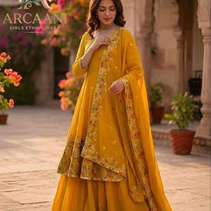 Puede incluir: Un vibrante conjunto de ropa étnica amarilla. El atuendo presenta una parte superior de manga larga, una falda en capas y una bufanda a juego, todos adornados con intrincados bordados y adornos. La imagen incluye el nombre de la marca "ARCAANI" y el texto "GIRLS ETHNIC WEAR".