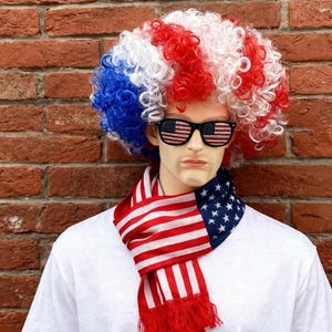 Op de afbeelding: Een mannequin in een patriottisch ensemble. Het heeft een krullende pruik in rood, wit en blauw, een zonnebril met lenzen met de Amerikaanse vlag en een sjaal met rood-witte strepen en blauwe sterren. De mannequin draagt een wit T-shirt.