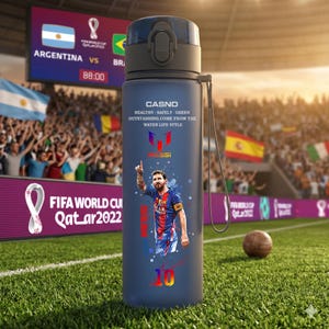 May include: A navy blue water bottle featuring an image of Lionel Messi and the text "CASNO". The bottle has a dark blue lid and a matching strap. The background shows a soccer stadium with a scoreboard and a soccer ball on the grass.