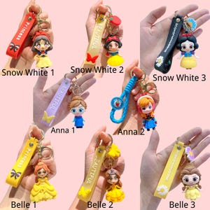 Puede incluir: Colecci&oacute;n de llaveros de personajes con Blancanieves, Anna y Bella. Cada llavero tiene una figura de personaje adjunta a una correa con texto. Las correas son de varios colores, incluyendo rojo, amarillo, negro y morado.