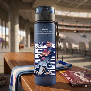 May include: A navy blue water bottle with a black lid and a black carrying strap. The bottle features a graphic of Kylian Mbapp&eacute; and the text "CASNO". The bottle also has the text "HEALTHY SAFELY GREEN OUTSTANDING COME FROM THE WATER LIFE STYLE".