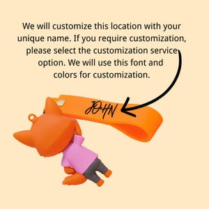 May include: Orange fox keychain with a pink shirt and gray pants. The keychain has an orange strap with the name "JOHN" in black script. The text above the keychain says, "We will customize this location with your unique name."