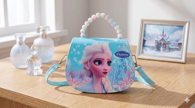 May include: A light blue purse featuring a graphic of Elsa from the movie Frozen. The purse has a beaded handle and a detachable shoulder strap. The word "FROZEN" is printed on the front. Other items on the wooden surface include perfume bottles and a framed picture.