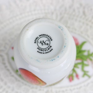 May include: A white porcelain teacup with a floral design, featuring the Royal Worcester Porcelain logo and "Made in England" text. The cup has a rounded shape and is set on a saucer with a floral pattern.