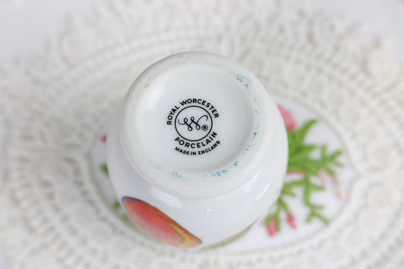 May include: A white porcelain teacup with a floral design, featuring the Royal Worcester Porcelain logo and "Made in England" text. The cup has a rounded shape and is set on a saucer with a floral pattern.