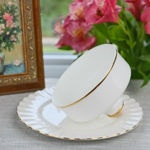 May include: A white teacup and saucer with a gold trim. The teacup is upside down on the saucer.