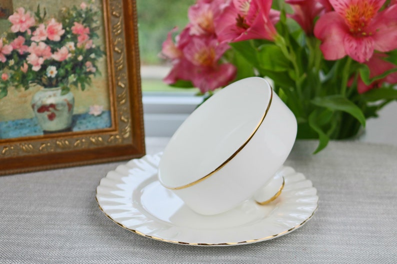 May include: A white teacup and saucer with a gold trim. The teacup is upside down on the saucer.