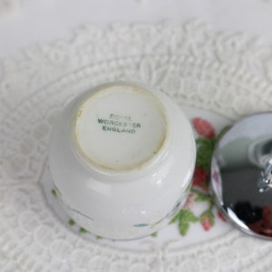 K&ouml;nnte beinhalten: Ein wei&szlig;er Eierbecher aus Keramik mit Blumenmuster und einem silbernen Deckel. Auf der Unterseite des Bechers steht "Royal Worcester England".