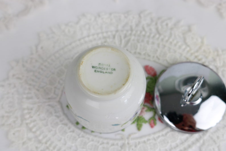 K&ouml;nnte beinhalten: Ein wei&szlig;er Eierbecher aus Keramik mit Blumenmuster und einem silbernen Deckel. Auf der Unterseite des Bechers steht "Royal Worcester England".