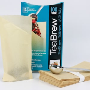Peut inclure: Une boîte de 100 filtres à thé en vrac TeaBrew. La boîte est bleue et blanche avec le texte "TeaBrew TheBrew TéBrew توليفة الشاي" et "100 Filters". Il y a aussi deux filtres individuels et une cuillère à thé en métal.
