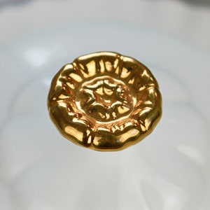 May include: A gold-colored, decorative knob with a floral design. The knob is round and has a raised center.