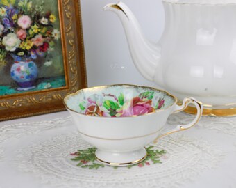 May include: A white teacup with a floral pattern and gold trim. The teacup is sitting on a white lace tablecloth.
