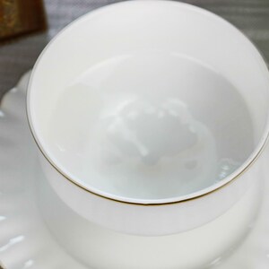 May include: A white porcelain teacup and saucer set with a gold rim. The cup and saucer are empty.
