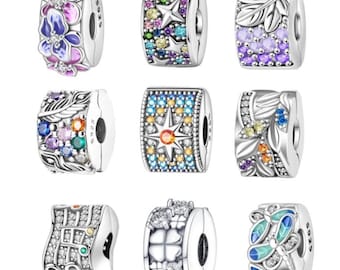 Puede incluir: Nueve abalorios plateados con diversos diseños. Los abalorios presentan motivos florales, de hojas, estrellas y geométricos, adornados con gemas de colores y esmalte. Cada abalorio tiene un agujero central para ensartar.