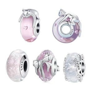 May include: A selection of silver charm beads. Two beads feature a cat design, one pink and one purple. Other beads include a pink bead with a bow, a white bead with glitter, and a white bead with a starfish design.