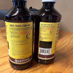 May include: Two brown liquid bottles with white caps and yellow labels. The labels include the text "Qualitest" and "ONE PINT (473 ml)". The bottles are filled with a dark brown liquid.