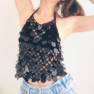 May include: Black halter top with a sequin design. The top has a crochet neckline and black sequins cascading down the front. It is worn with light blue denim jeans.