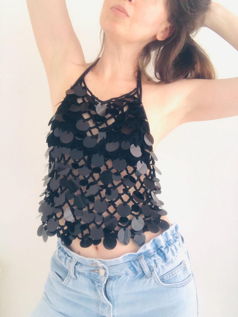 May include: Black halter top with a sequin design. The top has a crochet neckline and black sequins cascading down the front. It is worn with light blue denim jeans.