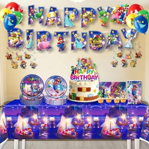 Può includere: Una scena di festa di compleanno con una tovaglia blu e decorazioni. Include una torta, piatti, palloncini e uno striscione con la scritta "Buon Compleanno". Le decorazioni presentano personaggi di un videogioco popolare.