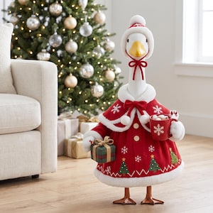May include: A decorative goose figurine wearing a red coat with white faux fur trim, a matching hat, and a cape. The coat features embroidered white snowflakes and green Christmas trees. It holds a red mug with a snowflake and a small gift box.