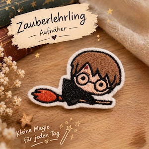 Könnte beinhalten: Ein gestickter Aufnäher, der eine Zeichentrickfigur mit braunen Haaren, runder Brille und einer blitzförmigen Narbe auf der Stirn zeigt, die auf einem Besen mit orangefarbenen Borsten reitet. Der Aufnäher hat einen weißen Rand und schwarze Fäden.