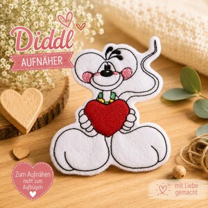 Pode incluir: Um emblema de tecido da ratinha Diddl em branco com contornos pretos, bochechas cor-de-rosa e um grande coração vermelho segurado nas mãos. O emblema inclui o texto Diddl AUFNÄHER e Zum Aufnähen nicht zum Aufbügeln, com um ícone de coração e a frase mit Liebe gemacht.