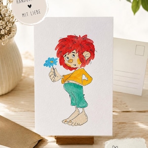 Könnte beinhalten: Eine weiße Postkarte mit einer Aquarellillustration einer Figur mit zerzaustem rotem Haar, gelbem Oberteil und grüner Hose, die eine kleine blaue Blume hält. Die Karte enthält den Text HANDGEMALT MIT LIEBE sowie POSTKARTE DIN A6.