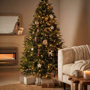 Op de afbeelding: Een hoge, volle kunstkerstboom met groene naalden, verlicht door warmwitte kerstverlichting. De boom is versierd met diverse ornamenten, waaronder notenkrakers, sterren en kerstballen, met verschillende ingepakte cadeaus aan de voet.
