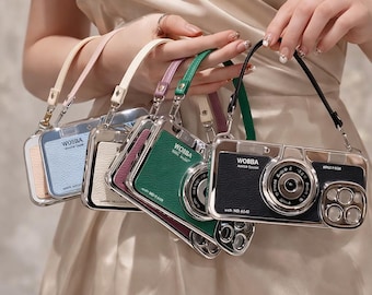 May include: A collection of camera-shaped phone cases in various colors, including black, green, blue, and cream. Each case has a silver frame and a matching strap. The cases are held together, showcasing their design and style.