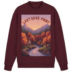 Könnte beinhalten: Burgunderfarbenes Sweatshirt mit einem pixeligen Landschaftsdesign und dem Text "LAST SAVE POINT". Das Bild zeigt einen Fluss, Häuser und Berge unter einem Sonnenuntergangshimmel, umgeben von Herbstbäumen. Das Sweatshirt ist ein Rundhals-Stil.