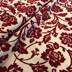 K&ouml;nnte beinhalten: Roter Samtstoff mit wei&szlig;em Hintergrund und einem floralen Muster. Der Stoff hat eine erhabene Textur und ein luxuri&ouml;ses Gef&uuml;hl.
