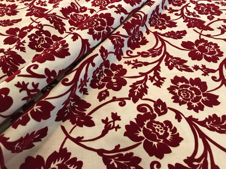 K&ouml;nnte beinhalten: Roter Samtstoff mit wei&szlig;em Hintergrund und einem floralen Muster. Der Stoff hat eine erhabene Textur und ein luxuri&ouml;ses Gef&uuml;hl.