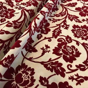 K&ouml;nnte beinhalten: Roter Samtstoff mit wei&szlig;em Hintergrund und einem floralen Muster. Der Stoff hat ein Damastdesign mit gro&szlig;en, stilisierten Blumen und Bl&auml;ttern.