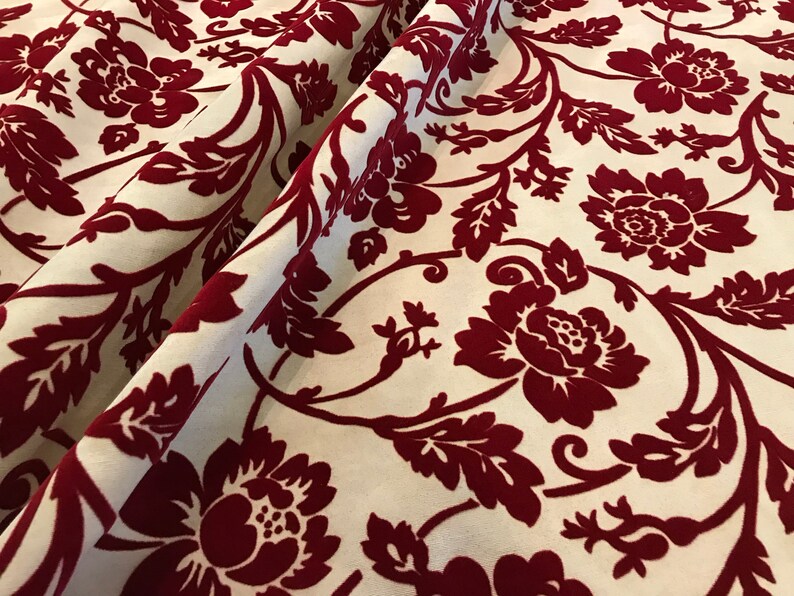 K&ouml;nnte beinhalten: Roter Samtstoff mit wei&szlig;em Hintergrund und einem floralen Muster. Der Stoff hat ein Damastdesign mit gro&szlig;en, stilisierten Blumen und Bl&auml;ttern.