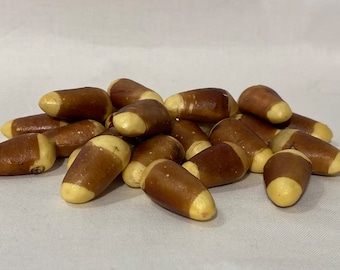 May include: A pile of Brazil nuts, each with a light tan end and a dark brown body. The nuts are oval-shaped and rest on a white surface. The image is well-lit, highlighting the texture and color of the nuts.