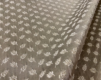 May include: A close-up of a fabric with a subtle, embossed pattern of white leaves on a brown background. The fabric is folded in half, showing the pattern on both sides.