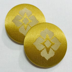 May include: Two oval-shaped gold fabric buttons with a white floral design.