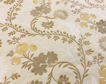 May include: A white fabric with a repeating pattern of brown and yellow floral designs. The fabric has a textured, woven look.