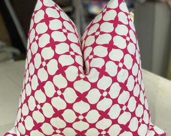 May include: A decorative throw pillow with a white background and a repeating pattern of magenta floral shapes. The pillow is square and appears to be made of a soft fabric, perfect for adding a pop of color to any room.