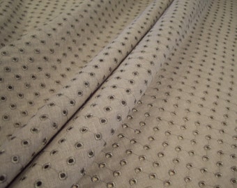 May include: A close-up of a beige fabric with a repeating pattern of small, circular holes. The fabric has a subtle texture and a slightly wrinkled appearance.