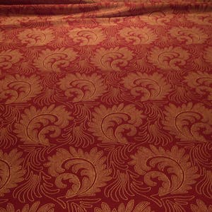 May include: Red fabric with a gold floral pattern. The pattern is a repeating design of stylized leaves and swirls.