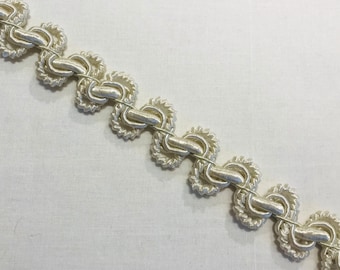 May include: A close-up of a white, decorative trim with a looped design. The trim is made of a soft, woven material and has a delicate, elegant look.