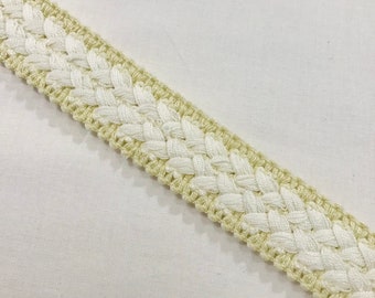 May include: A close-up of a white and beige braided trim. The trim is made of two different colors of yarn, woven together in a simple pattern.