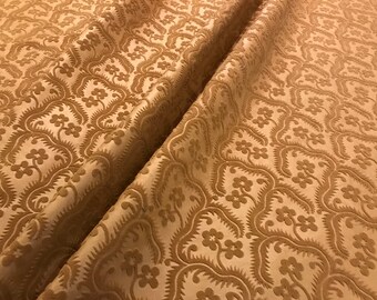 May include: A close-up of a beige fabric with a raised floral pattern. The fabric has a soft, velvety texture.