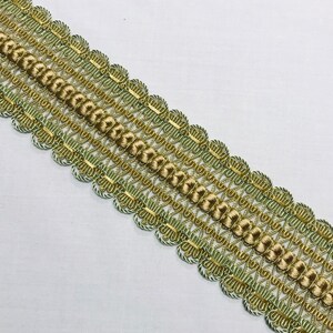 May include: A close-up of a decorative trim with a green and gold braided design. The trim is made of a soft, flexible material and has a delicate, intricate pattern.