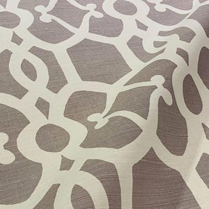 May include: Close-up of a fabric with a repeating pattern. The design features a white, looping, abstract motif against a muted, taupe-colored background. The fabric has a subtle texture, suggesting a linen or similar weave. The overall aesthetic is modern and elegant.