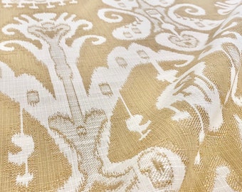 May include: Beige fabric with a white ikat pattern. The fabric has a subtle texture and a slightly wrinkled appearance.